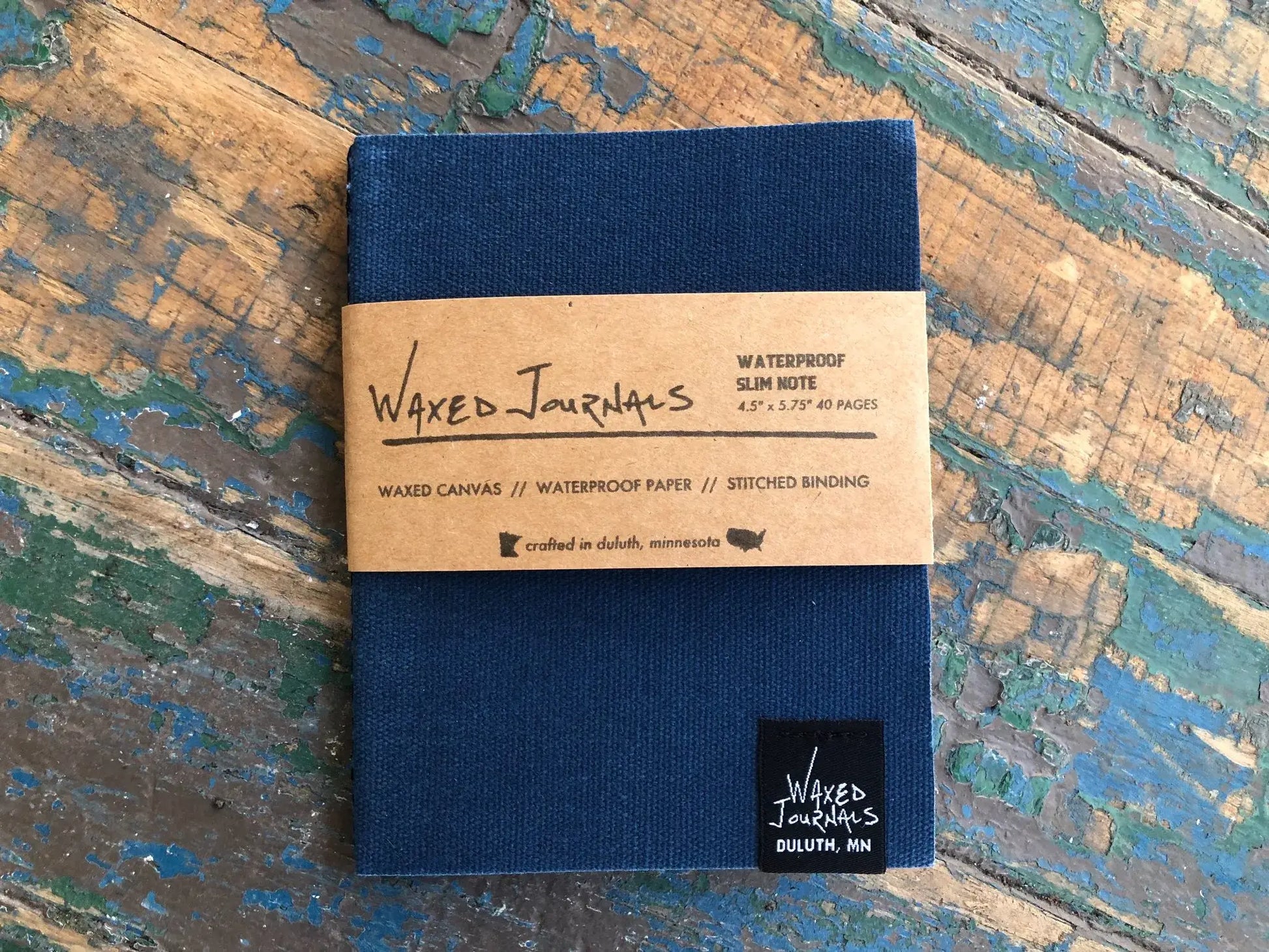 Blue waxed journal notebook in packaging on blue wood table.