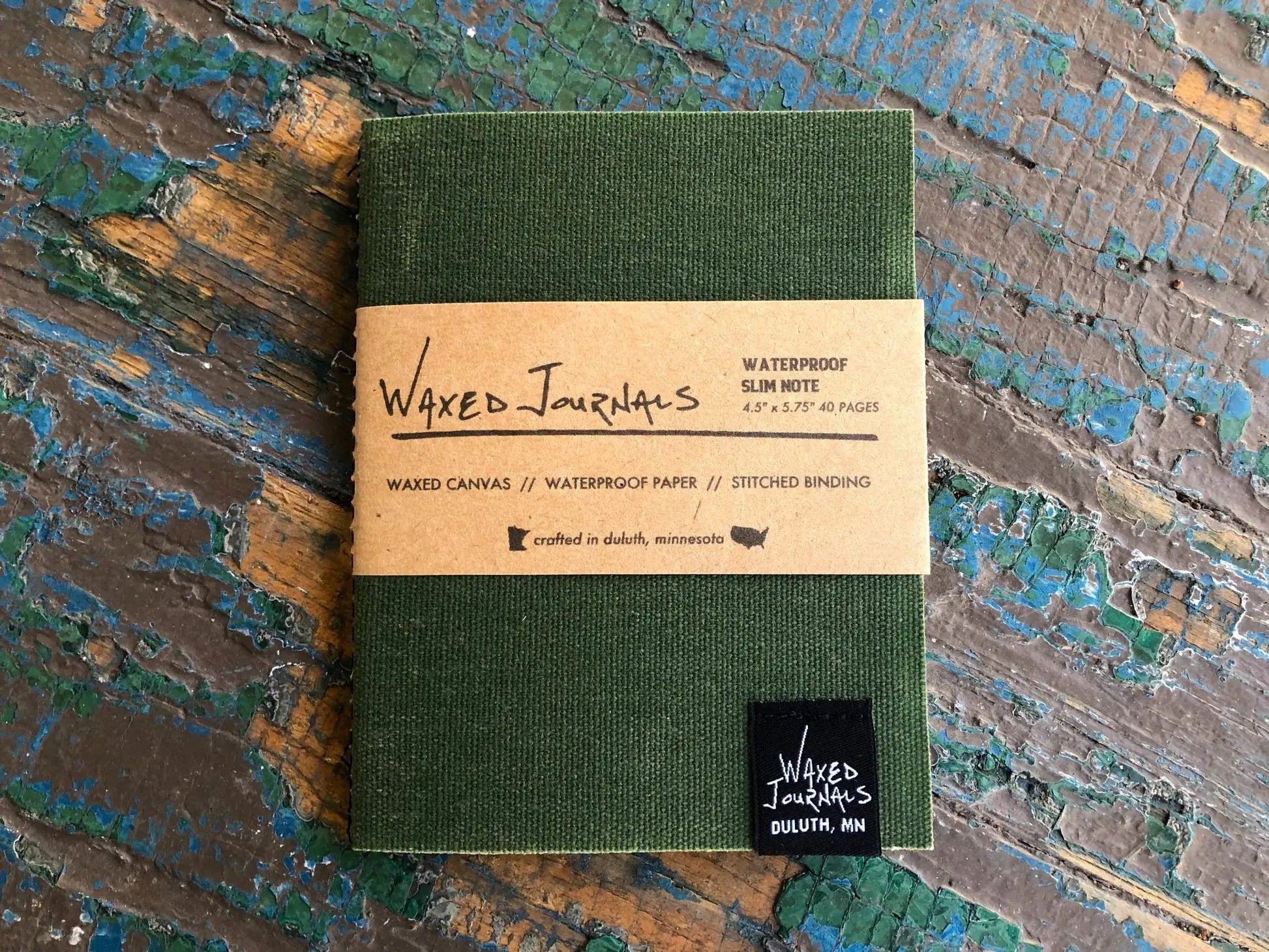 Green waxed journal notebook in packaging on a blue wood table.