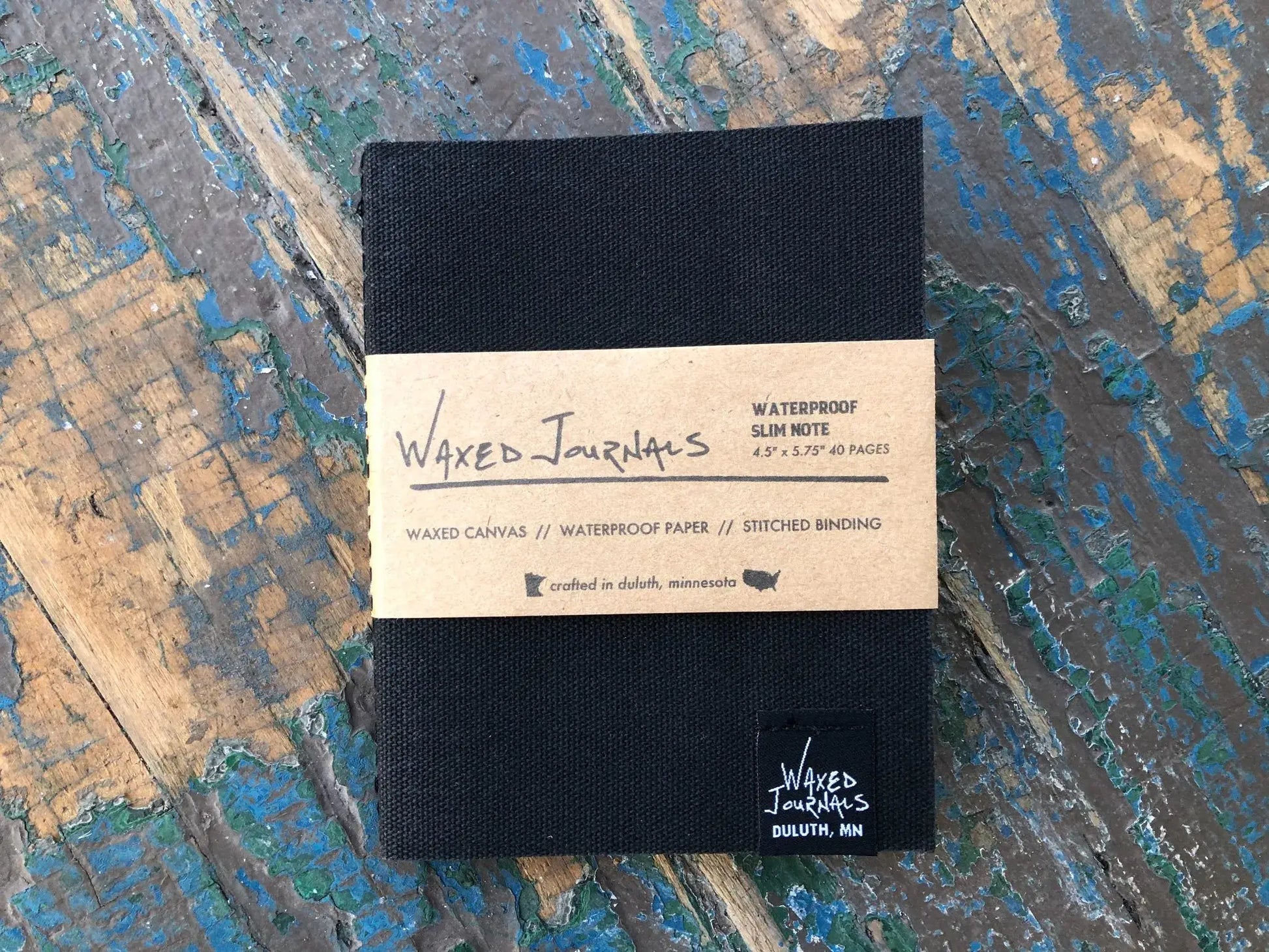 Black waxed journal in packaging on a blue wood table.