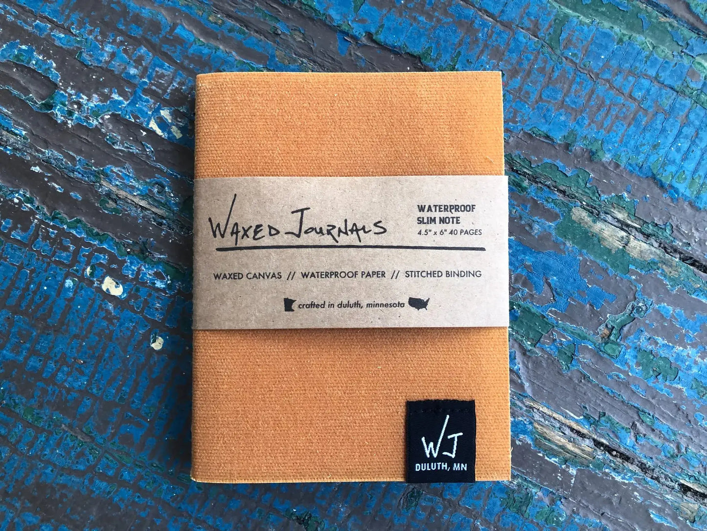 Yellow waxed journal notebook in packaging on a blue wood table.