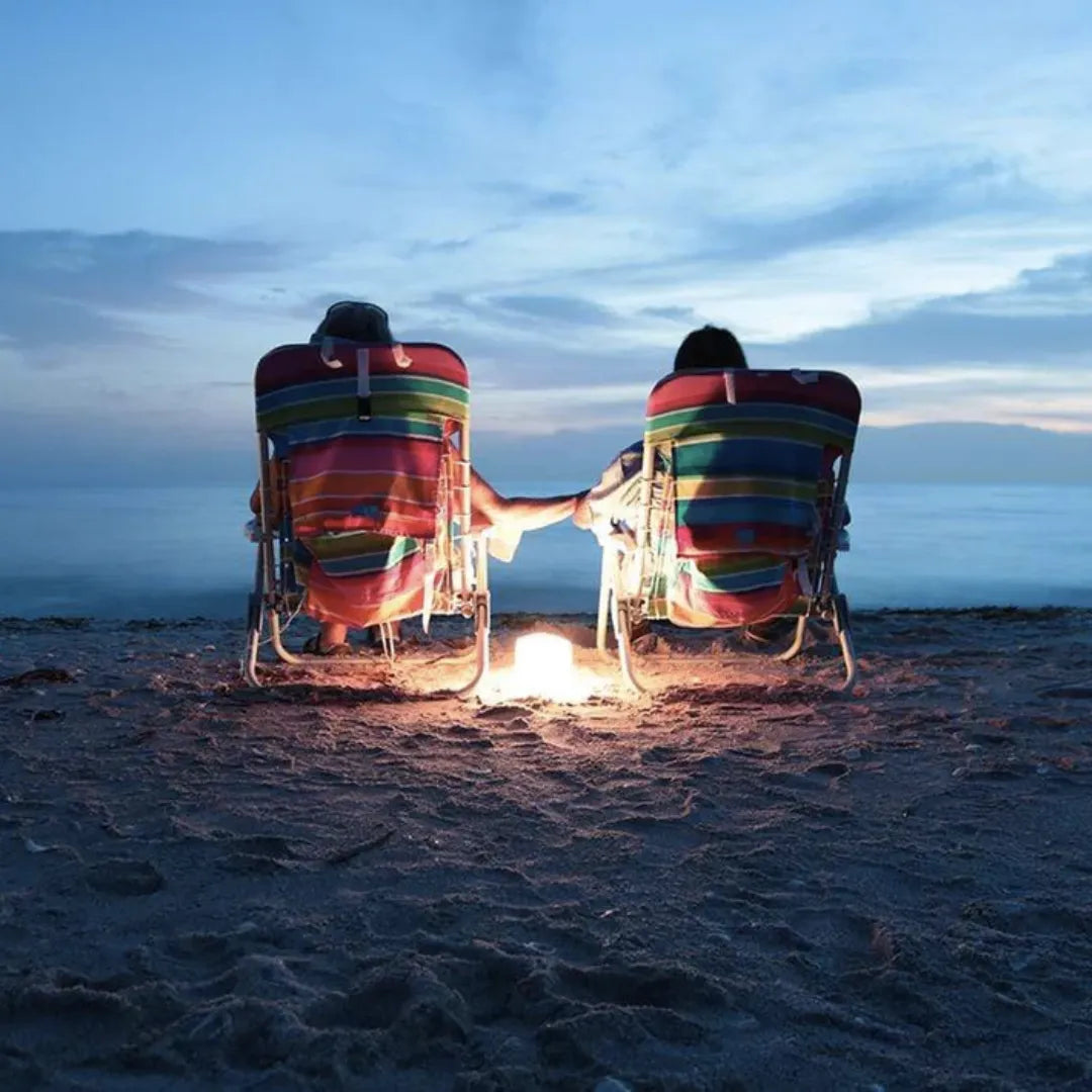 Two people on a beach with a lantern between them.
