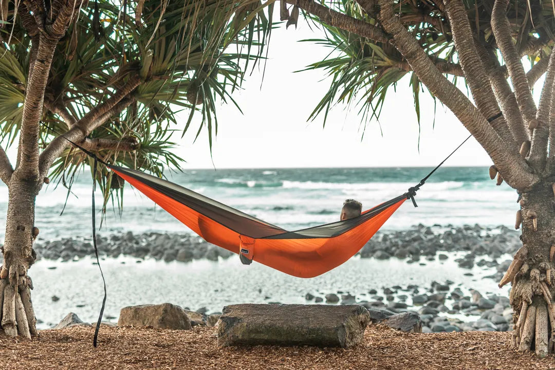 Man sitting in a orange and gray hammock on the beach.