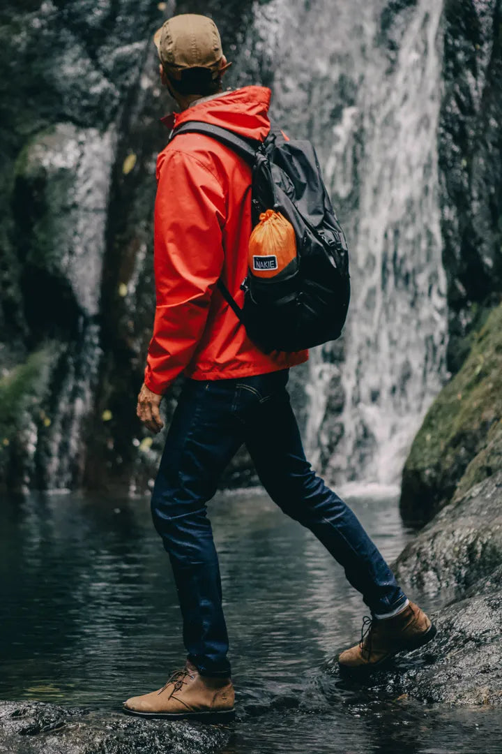 Man hiking by a waterfall with a orange and gray hammock bag.