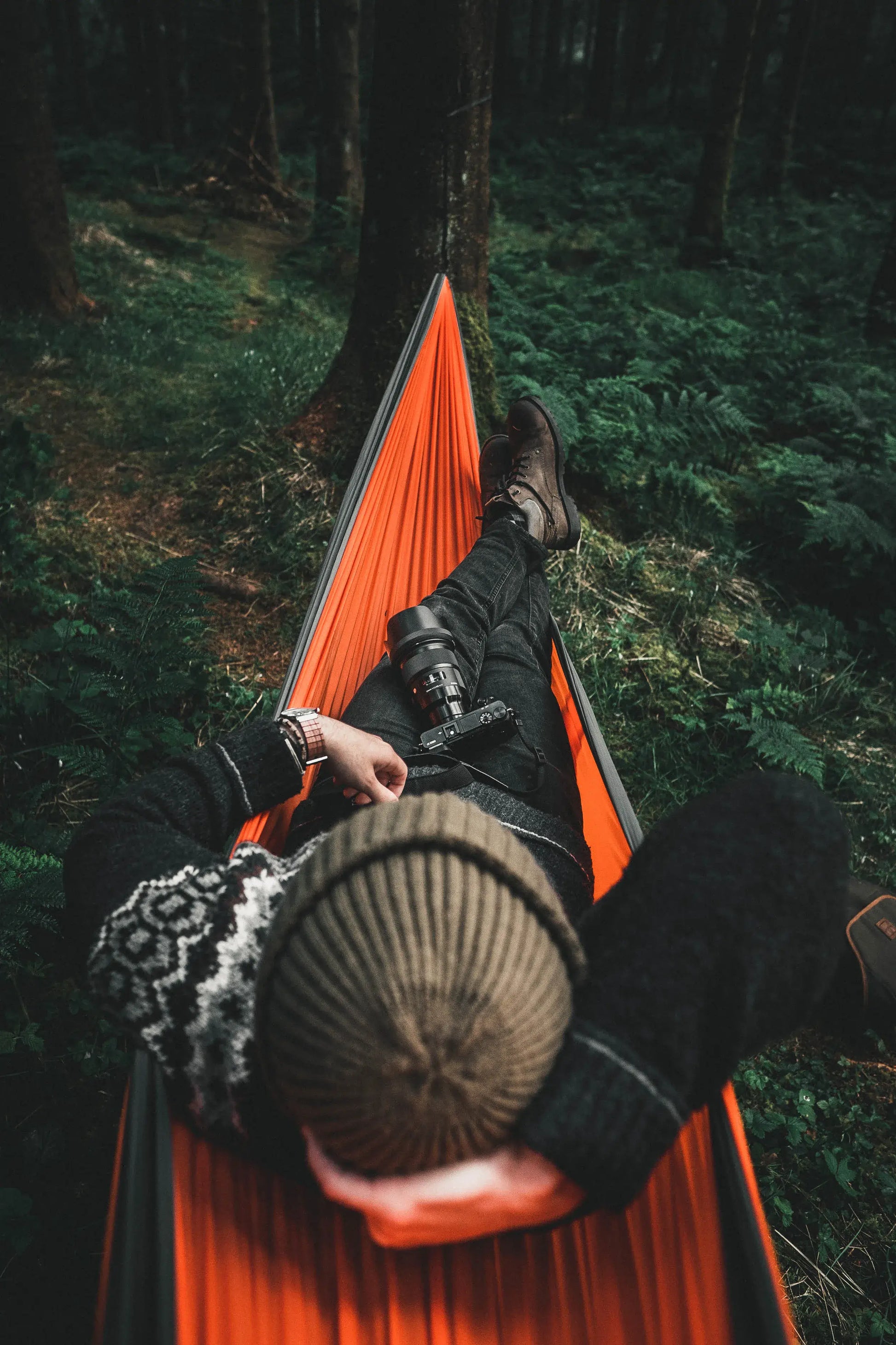 Person lying in a orange and gray hammock in the woods.