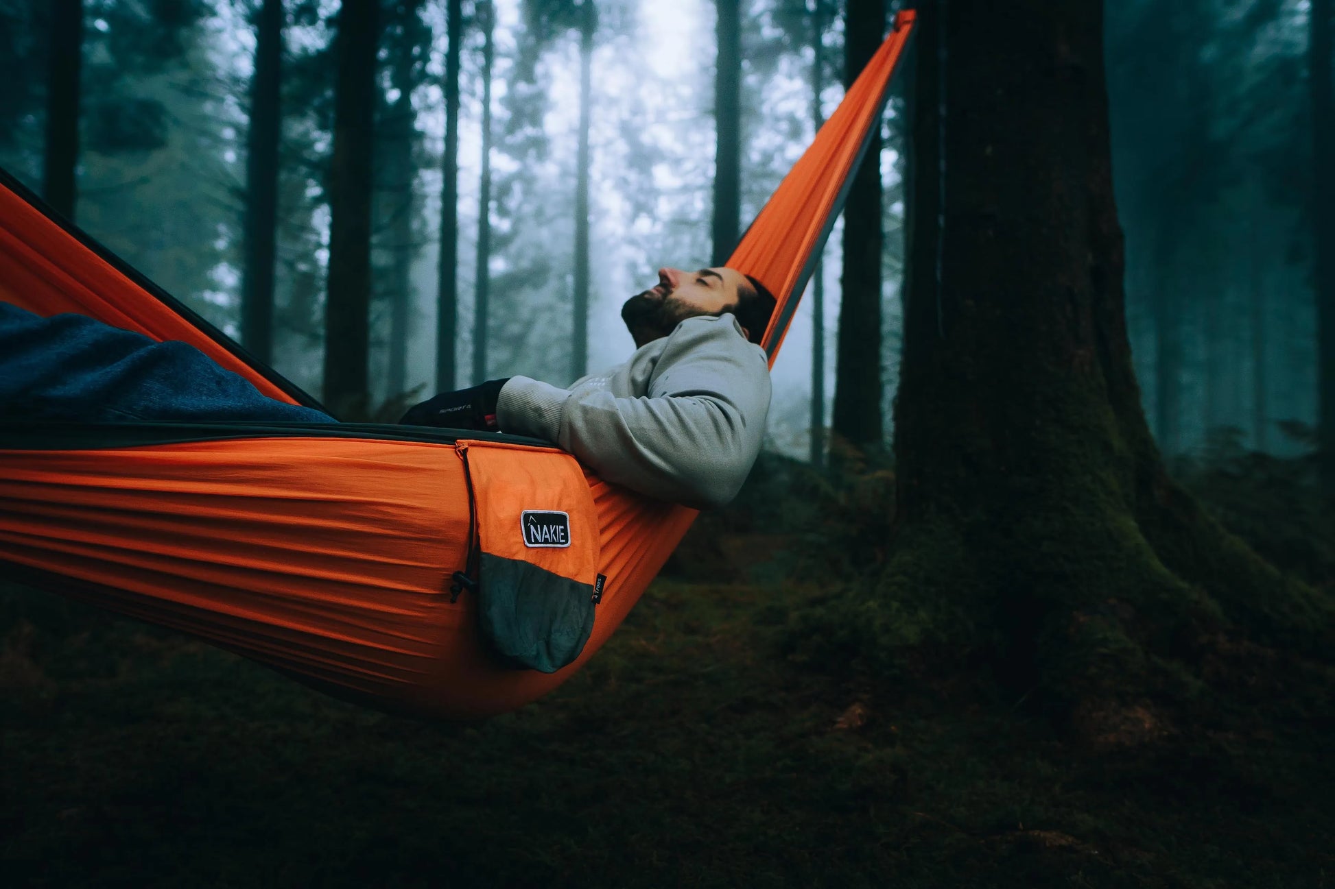 Man sleeping in a orange and gray hammock in the forest.