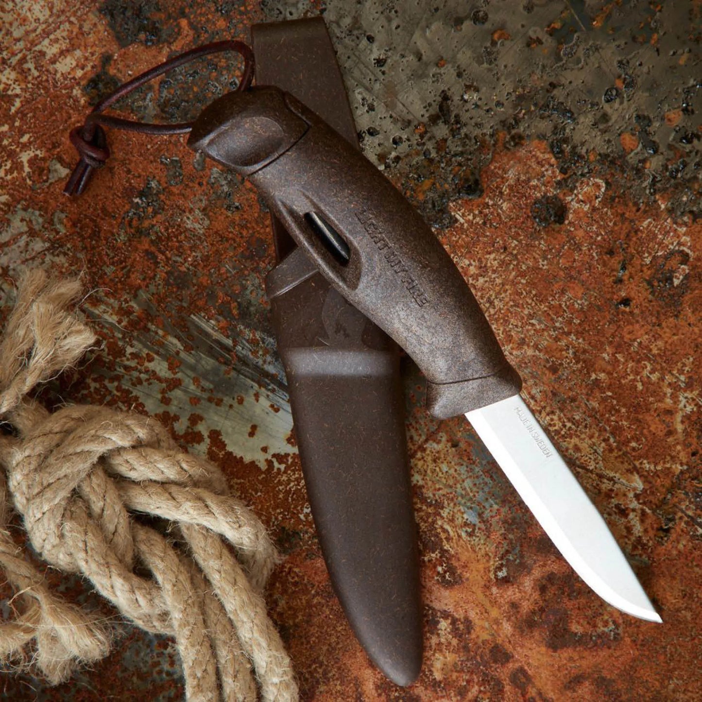 Brown knife and sheath next to rope on a rusty table.