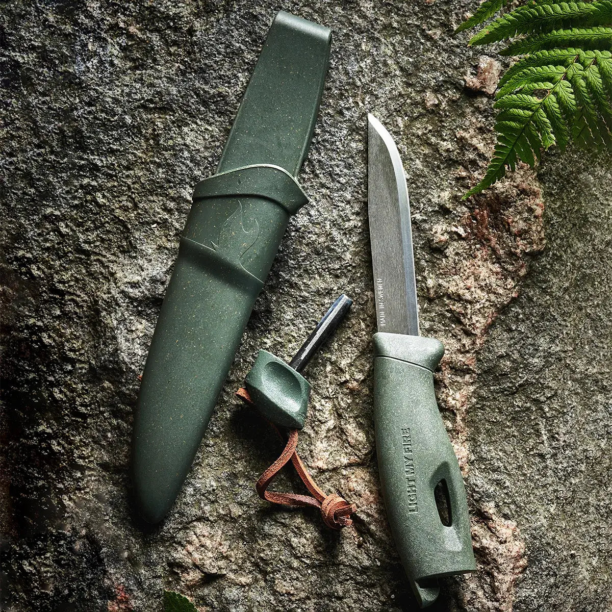 Green knife, shath and ferro rod on a rock.