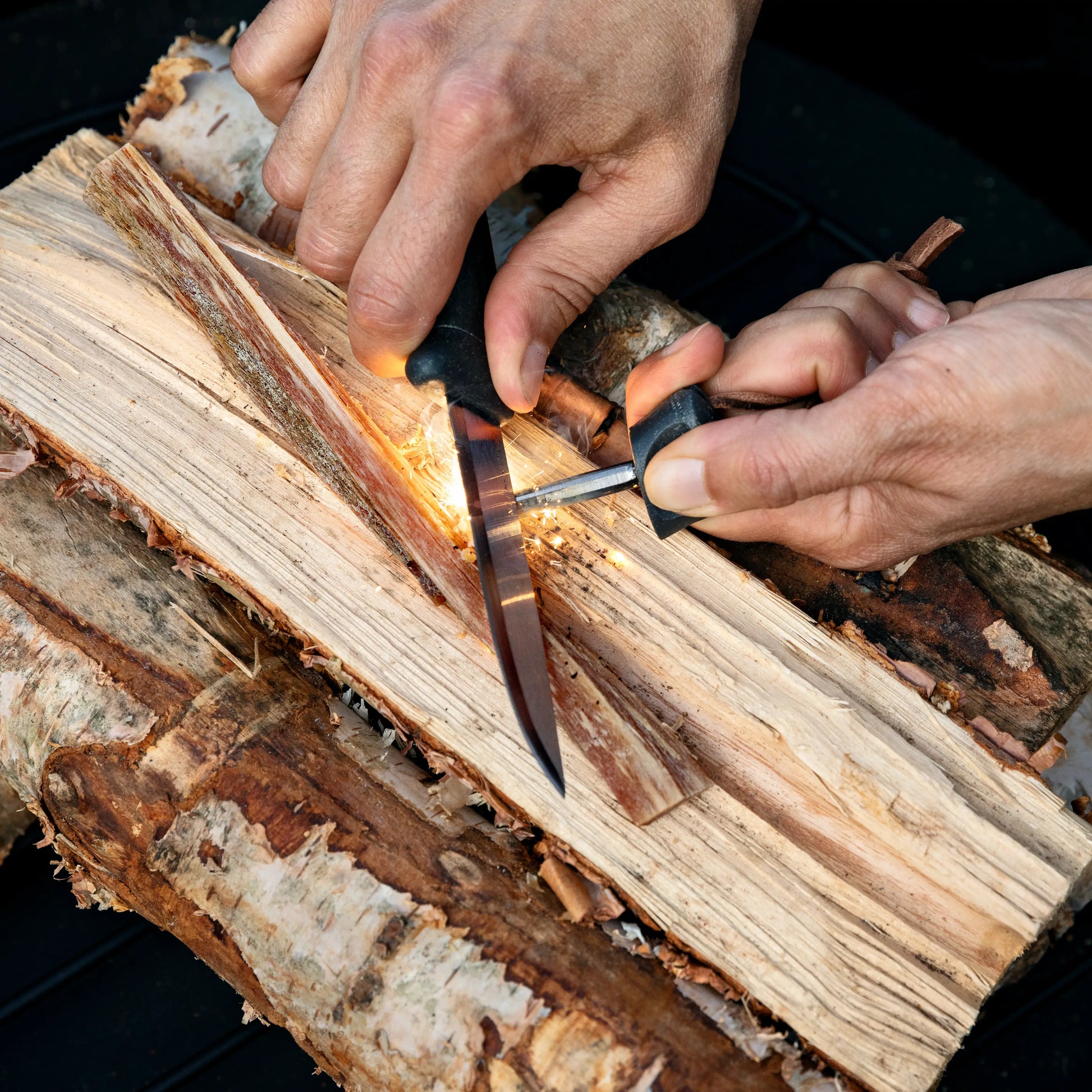 Making sparks with a knife and ferro rod on a wood log.