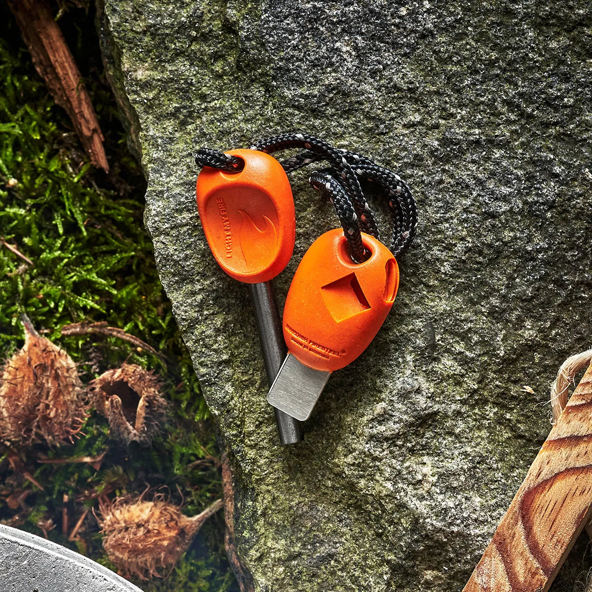 Orange ferro rod and striker outside on a rock.