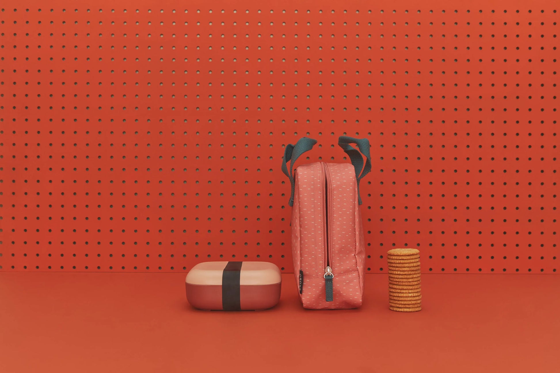 Blush and terracotta bento box next to bag and crackers.