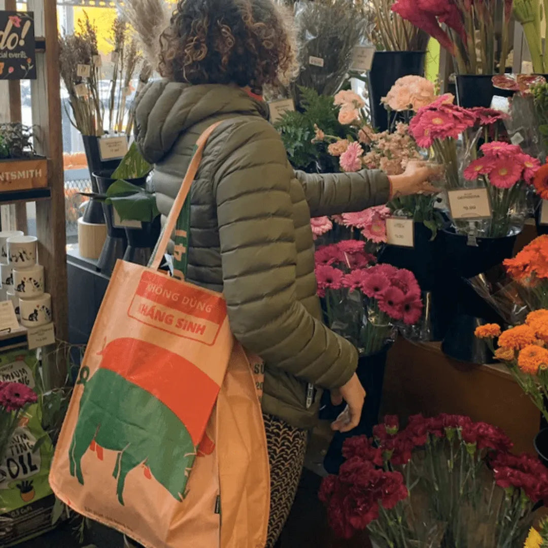Woman shopping for flowers wearing a tan tote bag with pigs on it.