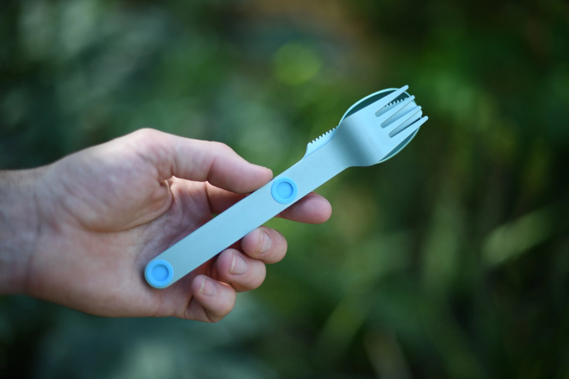Hand holding turquoise fork, knife and spoon connected.
