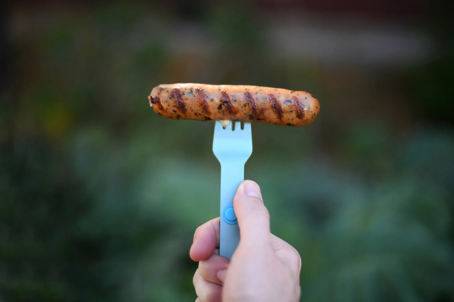 Turquoise fork holding a hotdog.