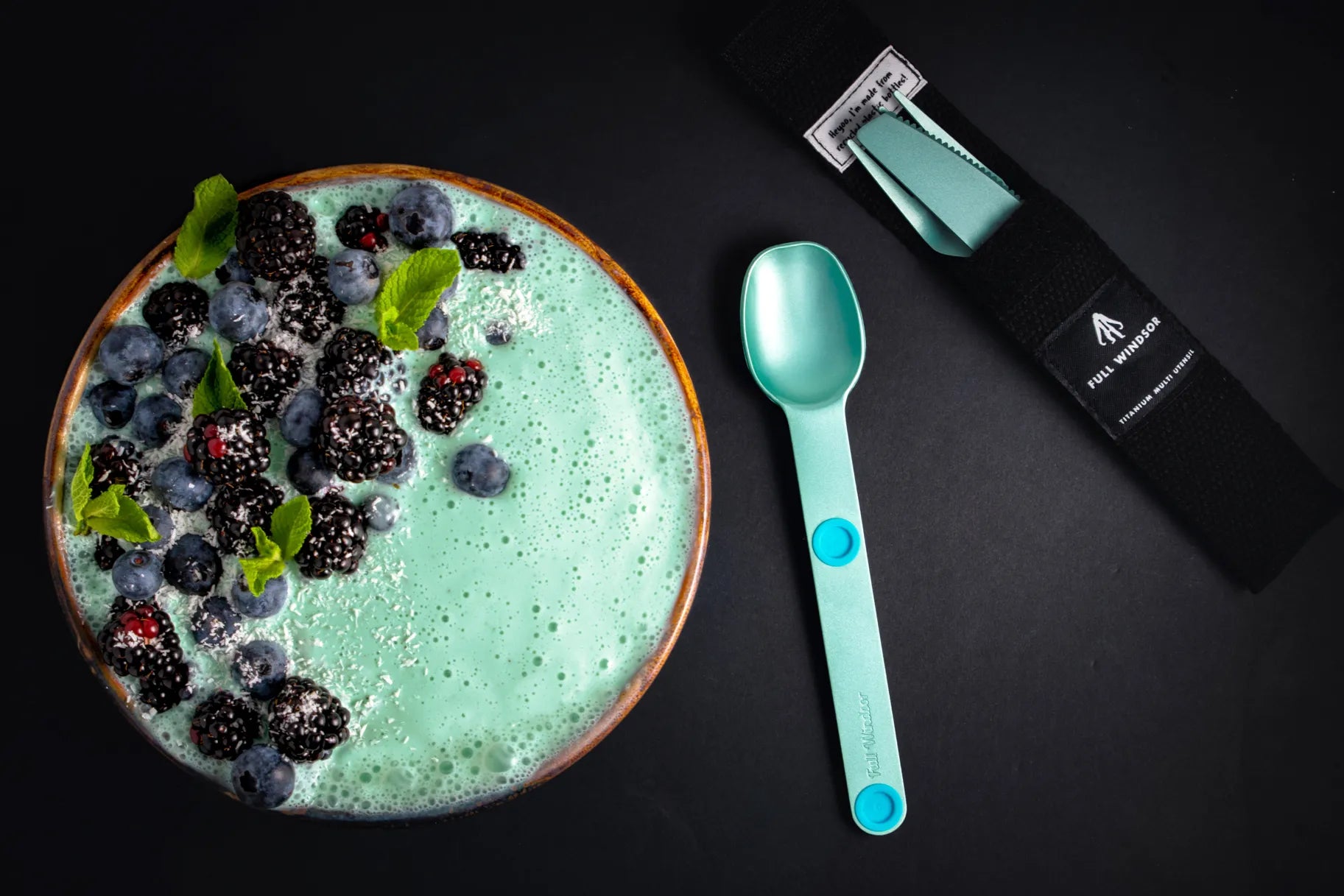 Turquoise fork, knife and spoon next to bowl of fruit and pudding.