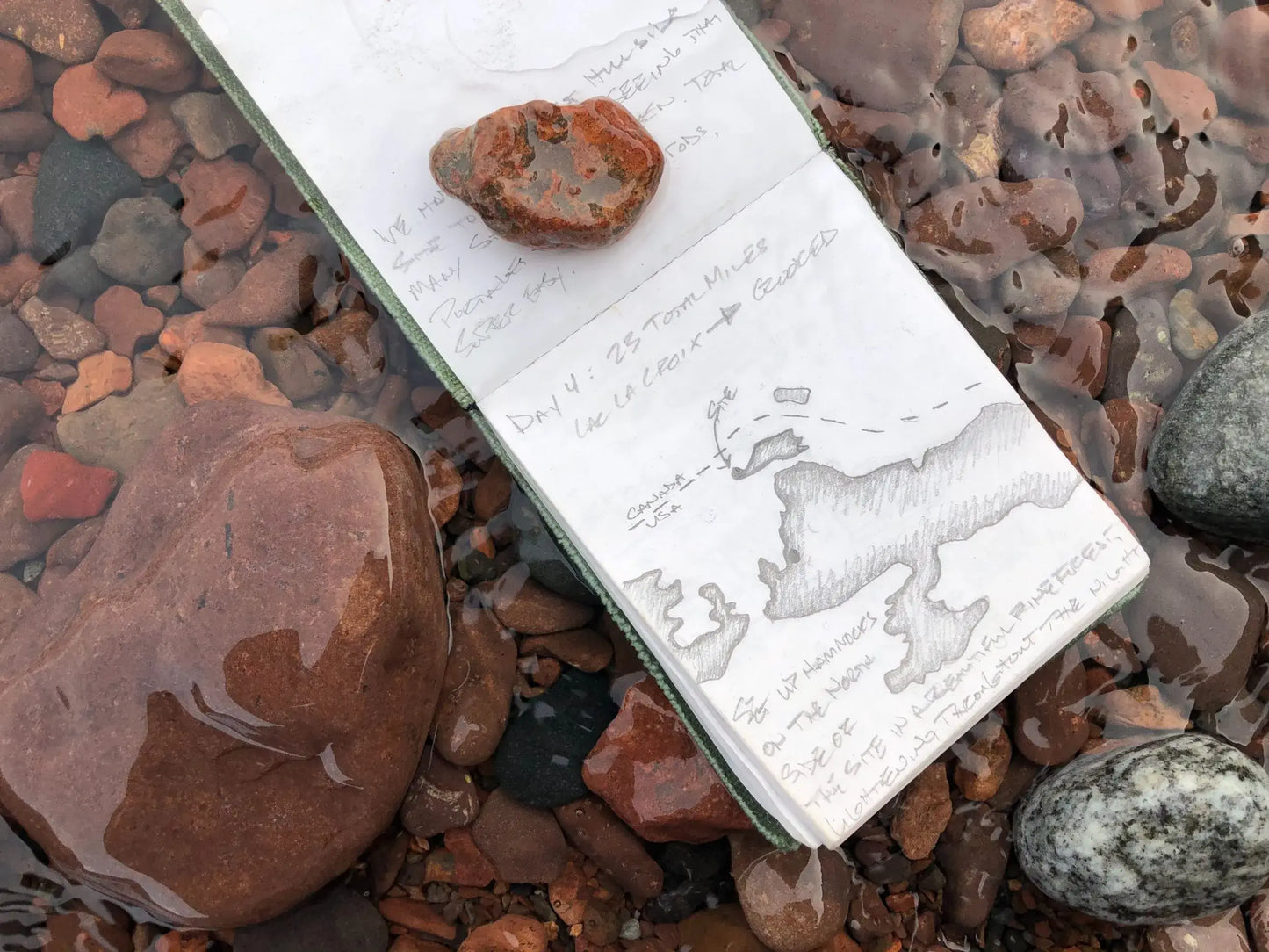 Notepad with writing on it in water with rocks.
