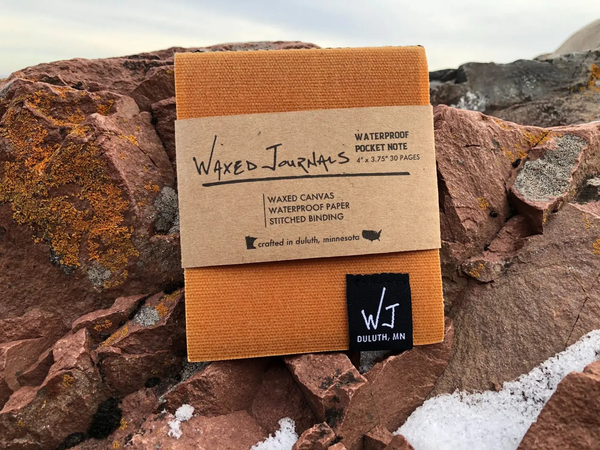 Yellow waxed journal notepad with packaging on rocks.