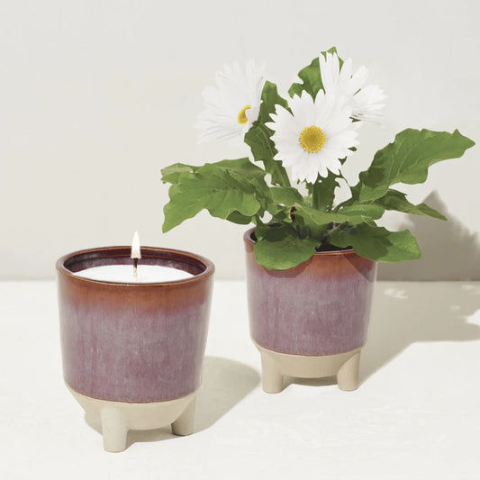 Two red pots, one with a candle and the other with wild flowers.