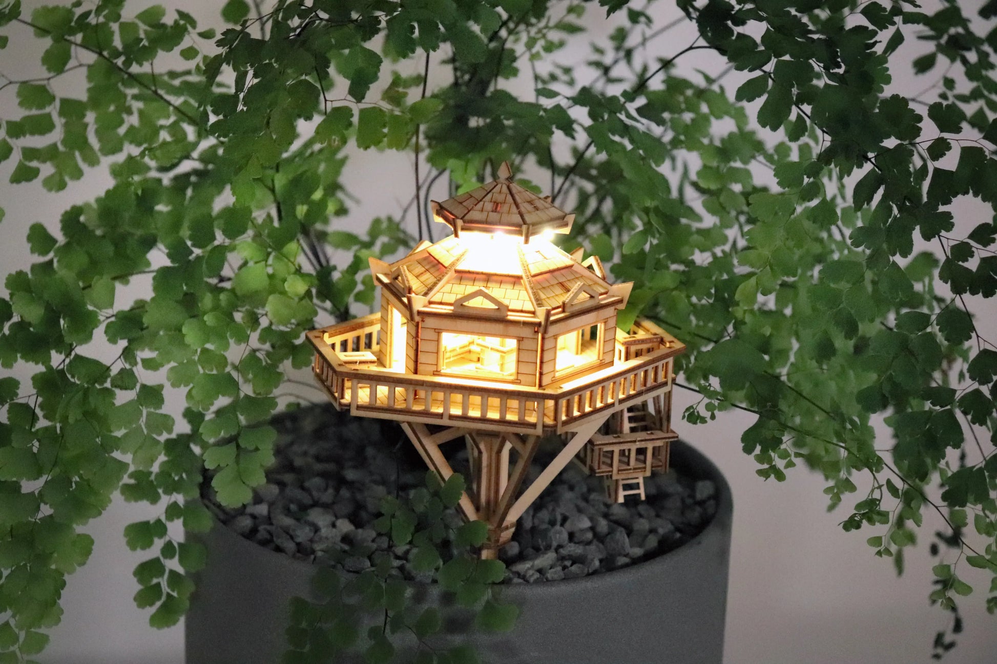 Small wooden treehouse with lights on in a potted plant.