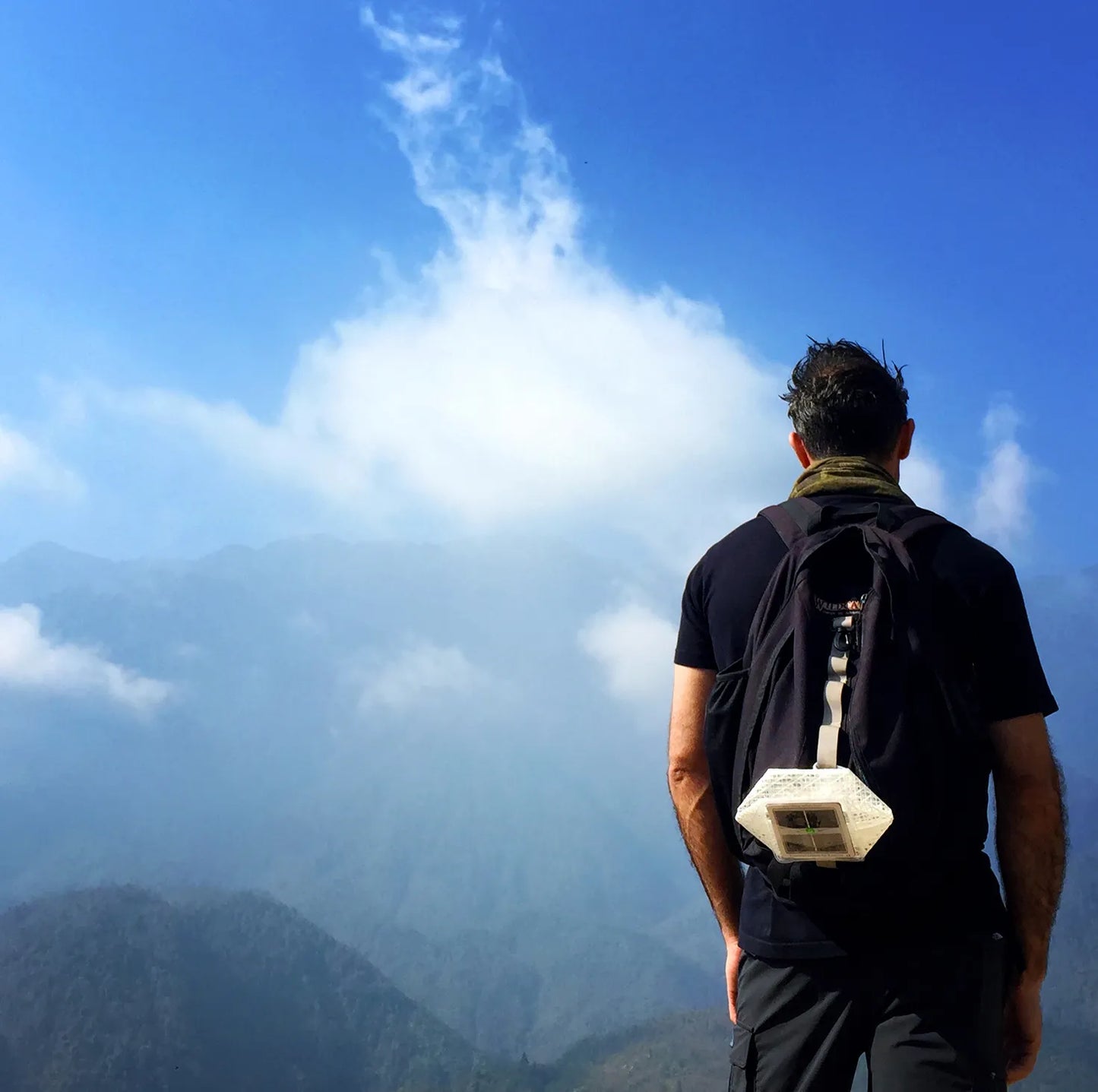 Man with backpack and a lantern attached looking at mountains.