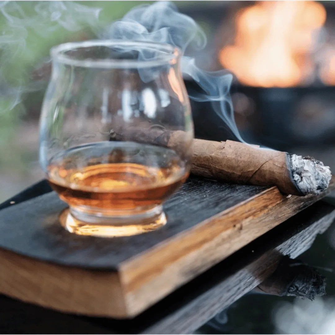Whiskey in a glass and a cigar on a coaster outside.
