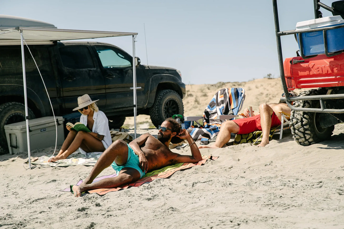 Friends laying on a beach next to vehicles.