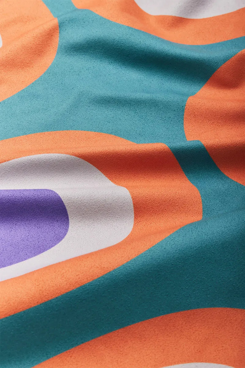 Close up of teal towel with orange, white and purple circles.
