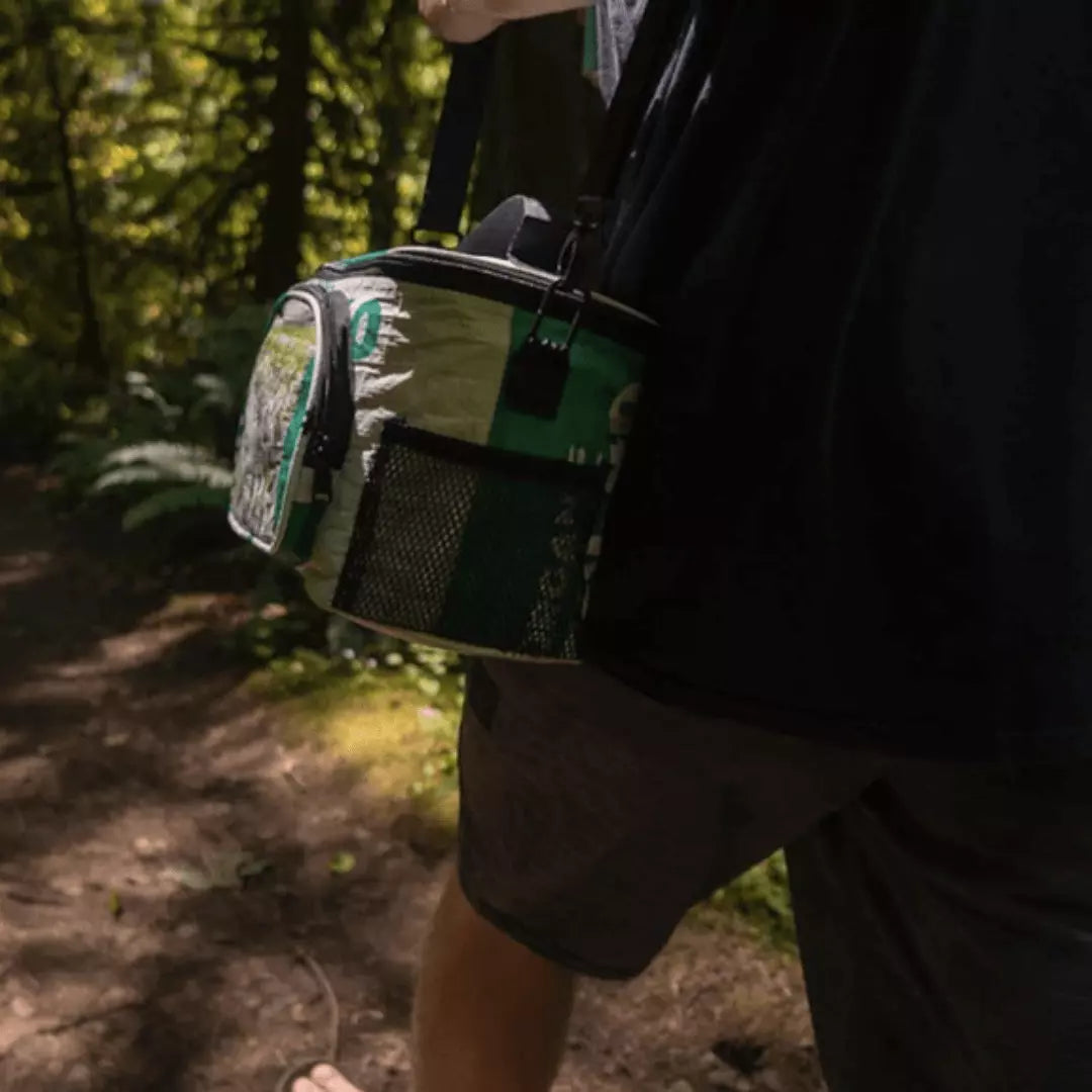 Man on a hike in the woods with a green and white cooler bag.