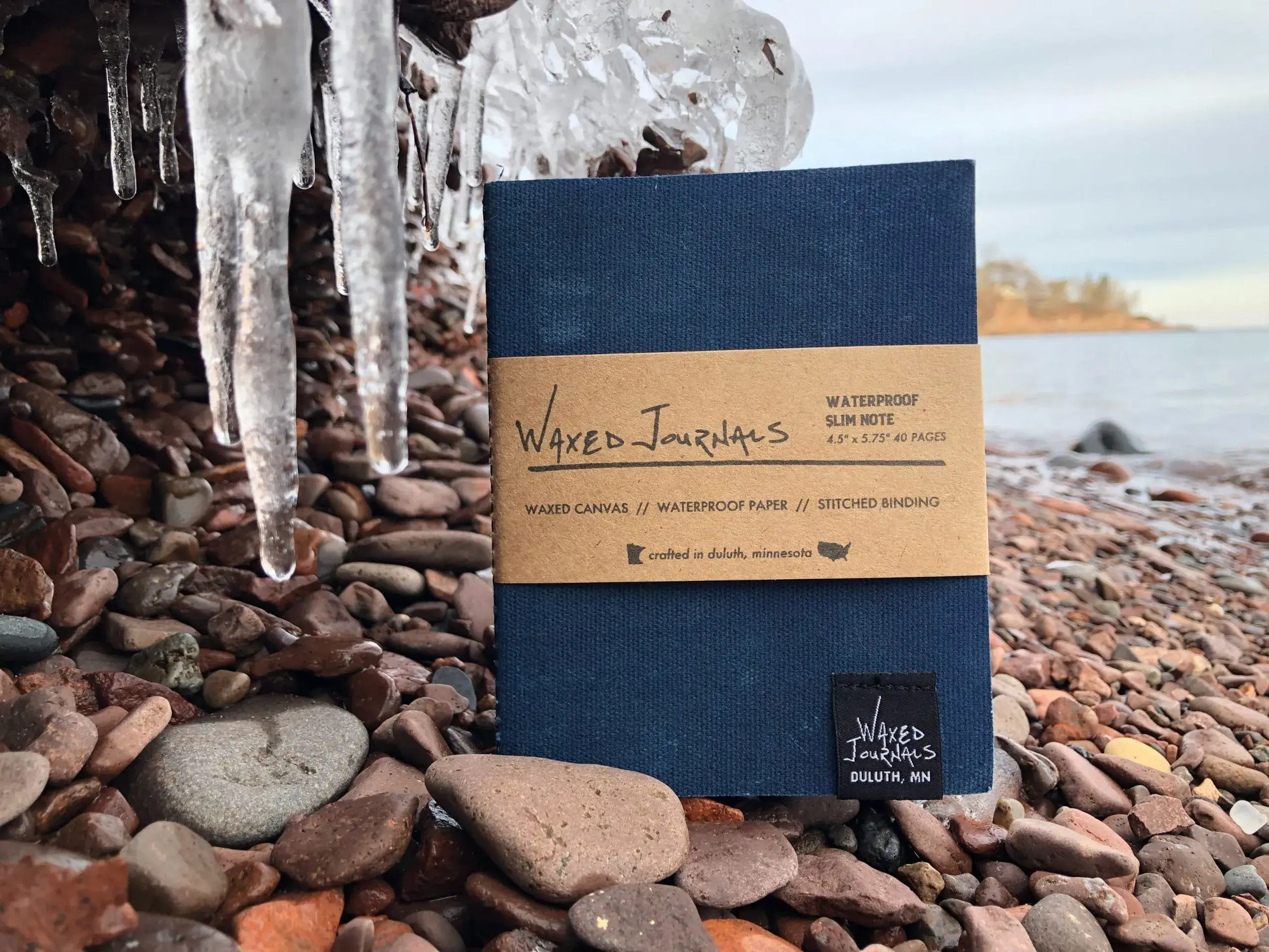 Blue waxed journal notebook in packaging outside on rocks next to ice.