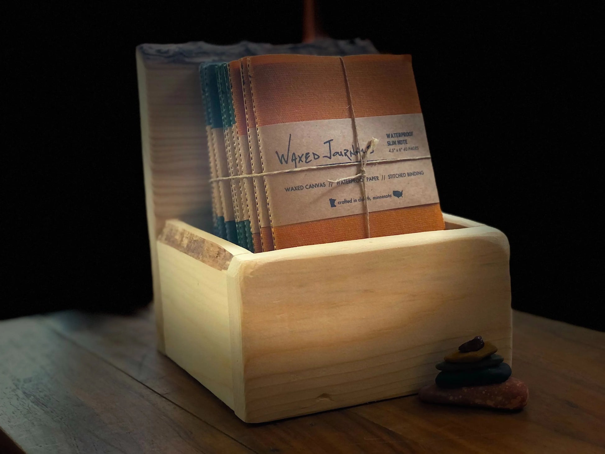 Multiple colors of waxed journal notepads in a wood box.