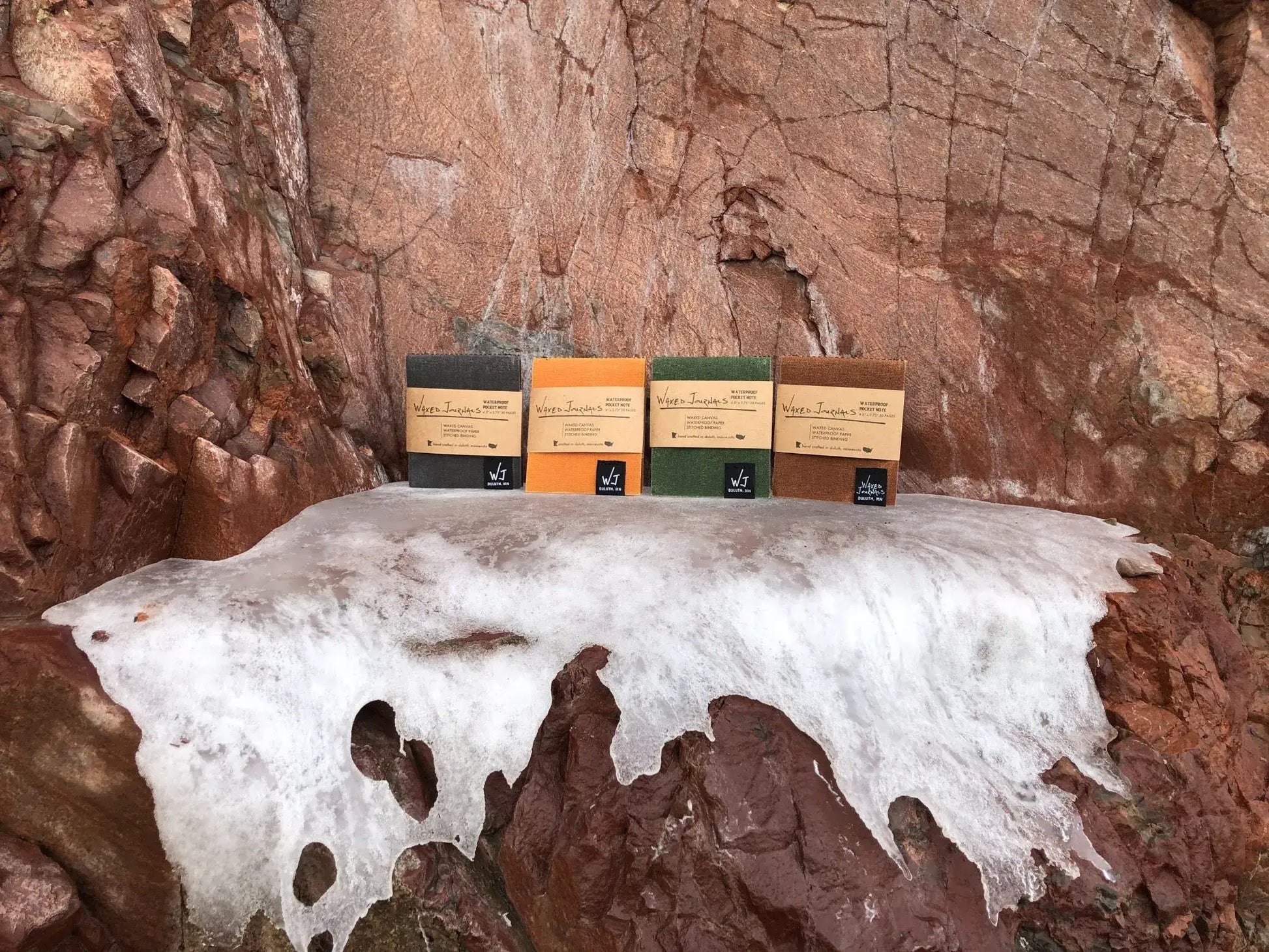 Multiple colors of waxed journal notepads on a rock wall with ice.
