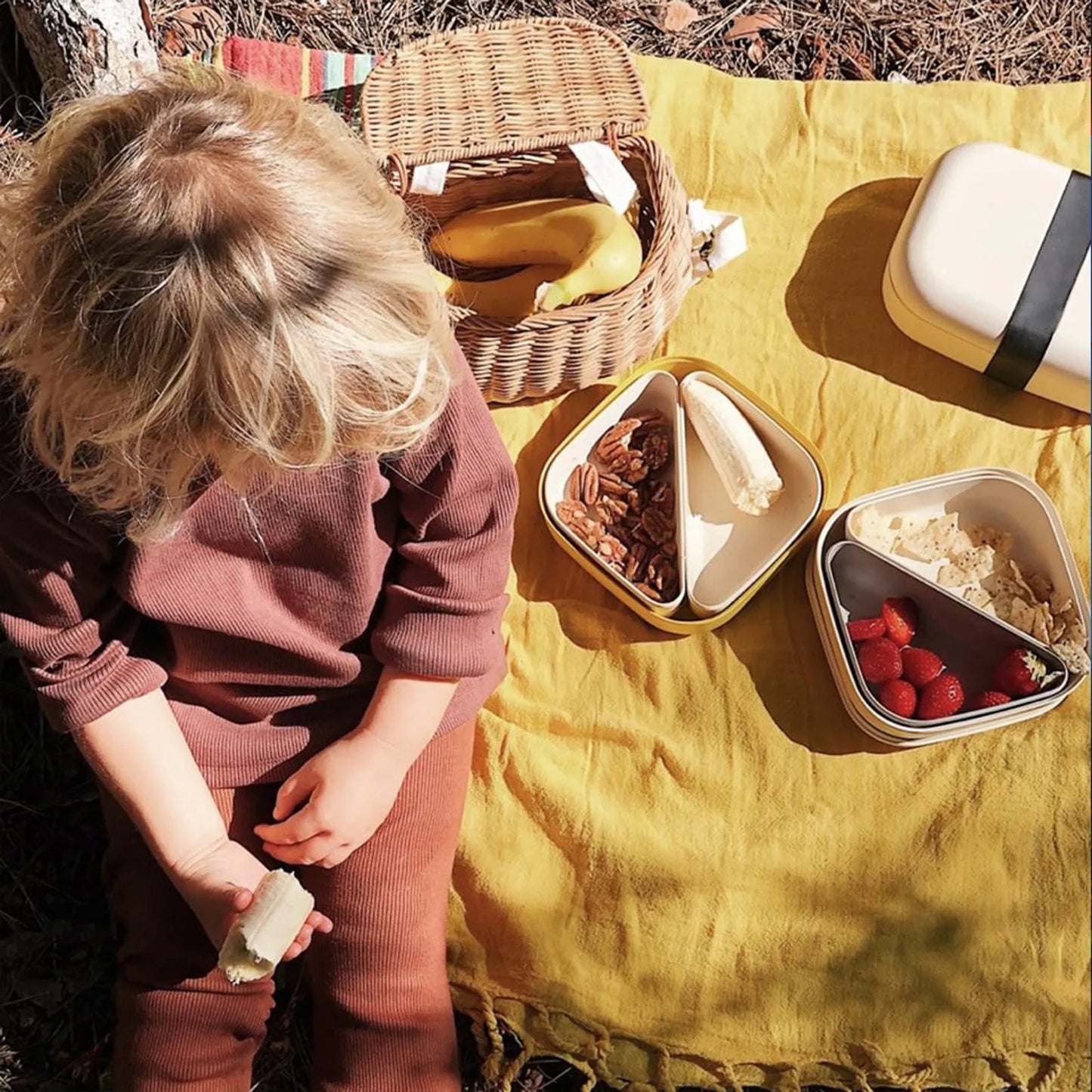 Child on a yellow picnic blanket with bento boxes and food.